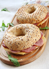 A tasty bagel with ham, cheese and seeds on a wooden board