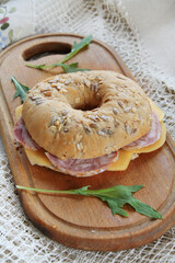 A tasty bagel with ham, cheese and seeds on a wooden board