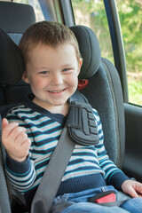 ittle boy sitting in car seat, smiling, looking at camera. The idea is the safety and convenience of children when driving, compliance with the rules for transporting children