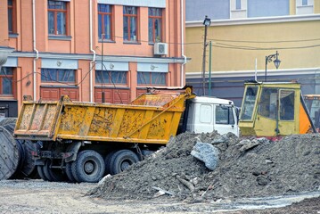 one large dump truck stands by a pile of gray sand at a construction site outside the brown wall of a building