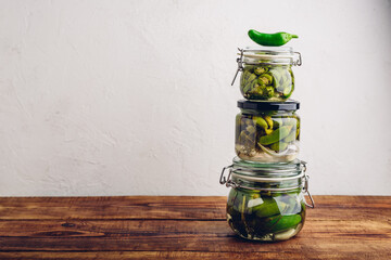 Three Glass Jars of Freshly Canned Jalapeno Peppers with Herbs and Garlic on Wooden Table. Copy Space