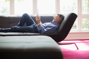 Senior man relaxing with digital tablet on living room sofa