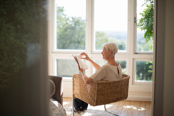 Senior woman relaxing and reading book in living room armchair