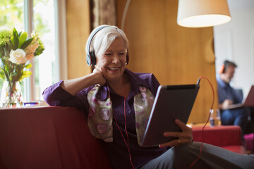 Happy senior woman using headphones and digital tablet on sofa