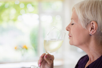 Serene senior woman smelling and tasting white wine