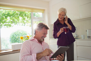 Happy senior couple using digital tablet and smart phone in kitchen