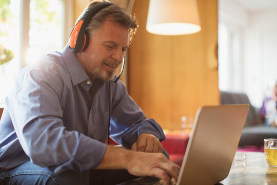 Senior man with headphones using laptop on living room sofa