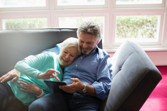 Happy senior couple cuddling and using digital tablet on sofa
