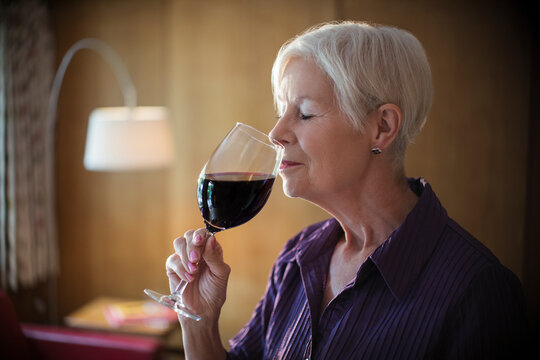 Serene senior woman smelling and tasting red wine