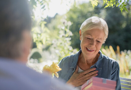 Happy senior woman receiving gift from husband on sunny patio