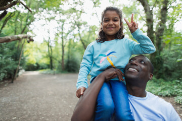 Portrait father carrying daughter gesturing peace sign in woods