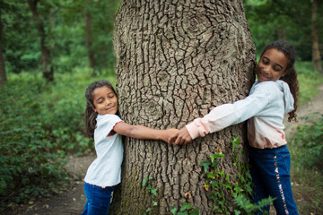 Serene sisters hugging tree trunk in woods