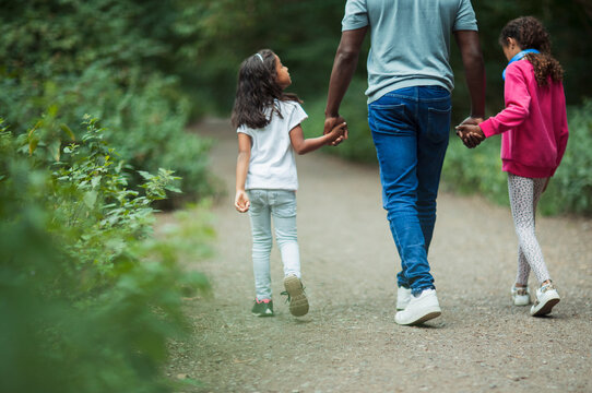 Father and daughters holding hands walking on path in park