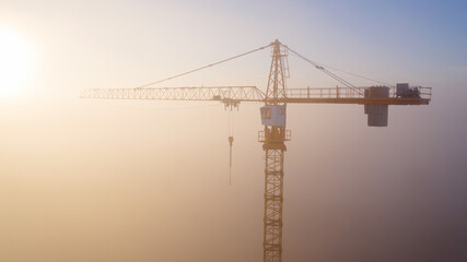Construction cranes at dawn in the morning mist.