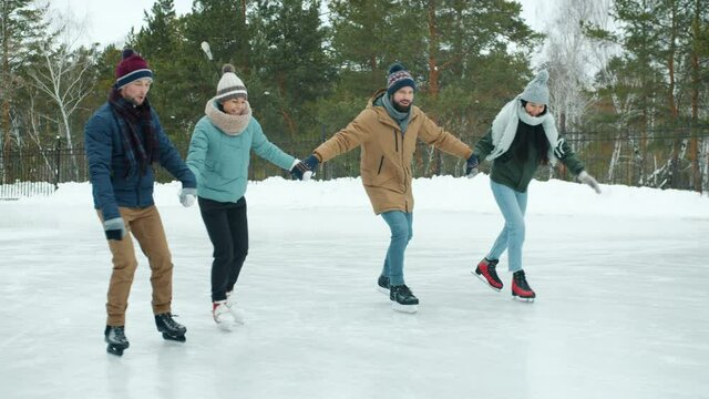 Multi-ethnic group of men and women Asian and Caucasian ice-skating in park in winter having fun together. Friendship and outdoor sports concept.