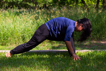 Fototapeta na wymiar Young Hispanic woman practicing yoga outdoors in a park with trees, very concentrated and relaxed