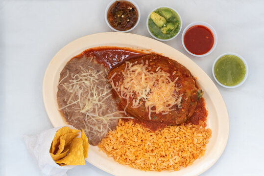 Overhead view of hearty meal of chile relleno, rice, and beans with chips and salsa tempts the taste buds to eat the entire meal.