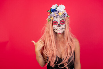 Lovely young beautiful woman wearing halloween make up over red background pointing aside with...