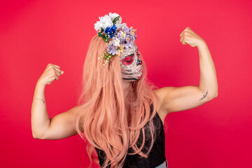 young beautiful woman wearing halloween make up over red background showing arms muscles smiling...