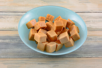 Chewy caramel candy squares in blue dessert bowl on table