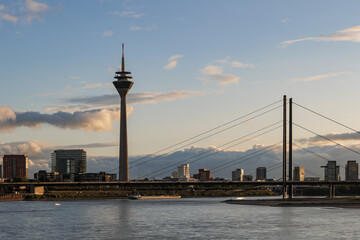 Fototapeta na wymiar Outdoor scenery of city skyline, downtown district, Rhein tower, suspension bridge and Rhine River against beautiful golden sunset sky in Düsseldorf, Germany. 
