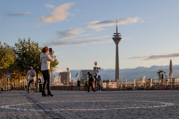 Selective focus on ground with circle symbol for caution peoples for Social Distancing from epidemic of COVID-19 at Burgplatz and defocus of woman take picture during sunset in Düsseldorf, Germany.