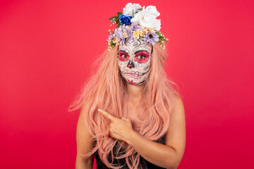 Young beautiful woman wearing halloween make up over red background. Pointing aside worried and nervous with forefinger, concern and surprise concept.