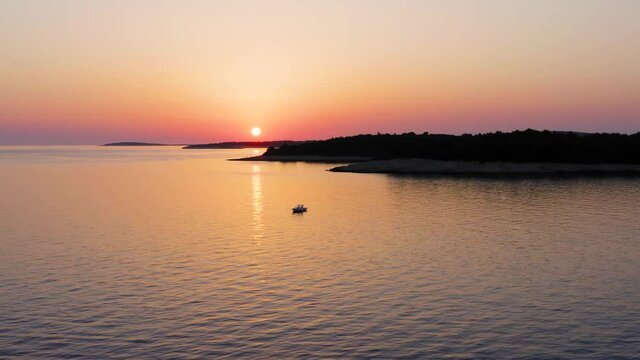 Scenic Beauty Of Golden Sunset Reflecting On The Calm Ocean Near Losinj Island, Croatia. Boat Floating On The Sea. - aerial pullback shot
