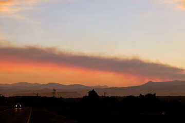 A car drives down a road in Denver Colorado with smoke from forest fires banded across the sky in the background, 2020