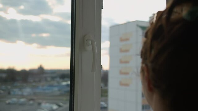 woman closes the window at home at sunset, cold in the evening