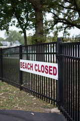 Beach Closed sign on metal fence in front of a lake