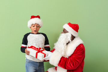 African-American Santa Claus giving present to cute little boy on color background
