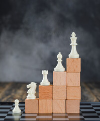 Business hierarchy concept with chessboard, figures, pyramid of wooden blocks on foggy and wooden background side view.