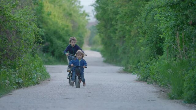 Brother riding bicycles on empty village road, children unequal competition