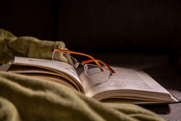 Open book with reading glasses on top and dark background in a cozy environment