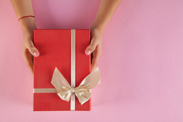 Gift box on an isolated pink background. Rectangular gift box. Woman's hands grabbed the box.