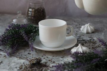 lavender tea in a white mug. Purple tea in a mug on a light background stands on the table next to lavender flowers. Dried lavender flowers are brewed in a Cup.