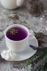 Obraz na płótnie Canvas lavender tea in a white mug. Purple tea in a mug on a light background stands on the table next to lavender flowers. Dried lavender flowers are brewed in a Cup.