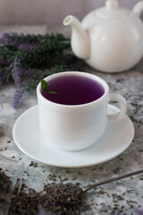 lavender tea in a white mug. Purple tea in a mug on a light background stands on the table next to lavender flowers. Dried lavender flowers are brewed in a Cup.