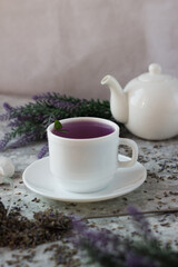 lavender tea in a white mug. Purple tea in a mug on a light background stands on the table next to lavender flowers. Dried lavender flowers are brewed in a Cup.