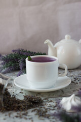 lavender tea in a white mug. Purple tea in a mug on a light background stands on the table next to lavender flowers. Dried lavender flowers are brewed in a Cup.