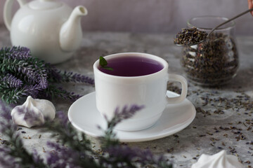 lavender tea in a white mug. Purple tea in a mug on a light background stands on the table next to lavender flowers. Dried lavender flowers are brewed in a Cup.
