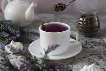 Obraz na płótnie Canvas lavender tea in a white mug. Purple tea in a mug on a light background stands on the table next to lavender flowers