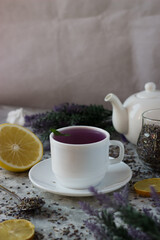 lavender tea in a white mug. Purple tea in a mug on a light background stands on the table next to lavender flowers. Dried lavender flowers are brewed in a Cup.