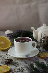 lavender tea in a white mug. Purple tea in a mug on a light background stands on the table next to lavender flowers. Dried lavender flowers are brewed in a Cup.