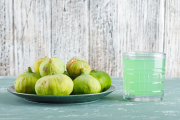 Green figs in a plate with drink side view on plaster and wooden background