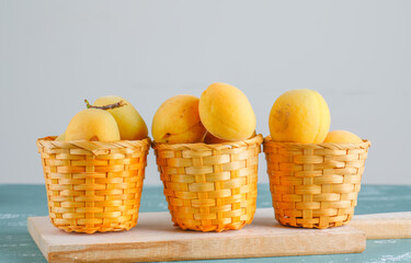 Apricots with cutting board in baskets on plaster and white background, side view.