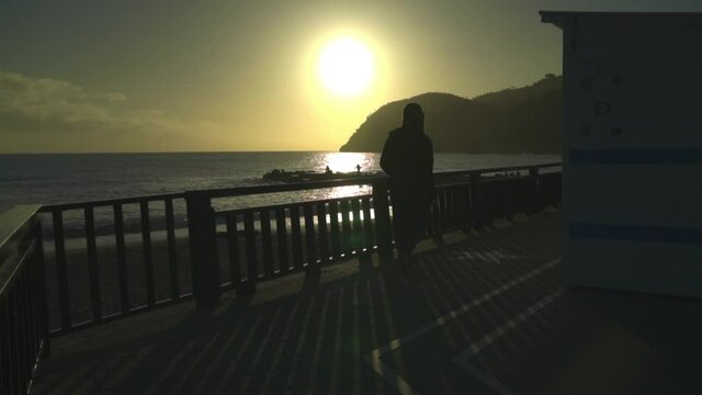 Woman walking on the boardwalk to the beach during sunset. Silhouette from behind