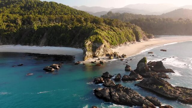 Beautiful Monro Beach during golden hour aerial pull back shot reveal scenic sandy beach and rock formation on New Zealand seaside, West Coast