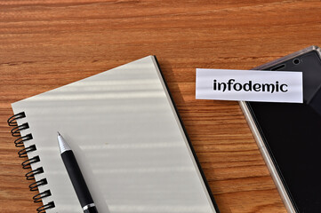 There is a card on the table with the word "infodemic" written on it, on a notebook. INFODEMIC is a term coined from information and pandemic.